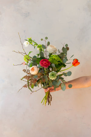 An arm holding an artfully designed wrapped floral bouquet 