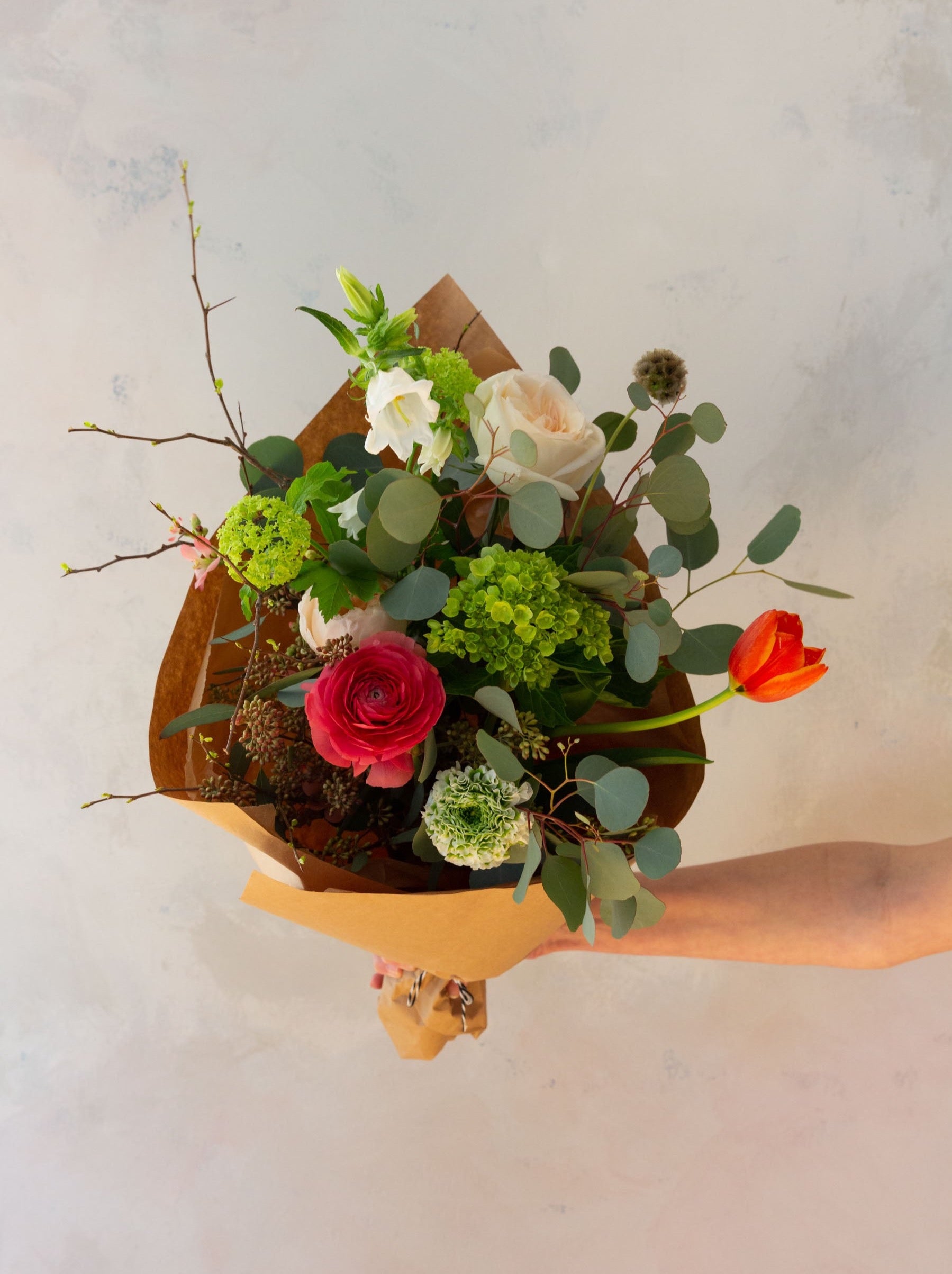 An arm holding an artfully designed wrapped floral bouquet 