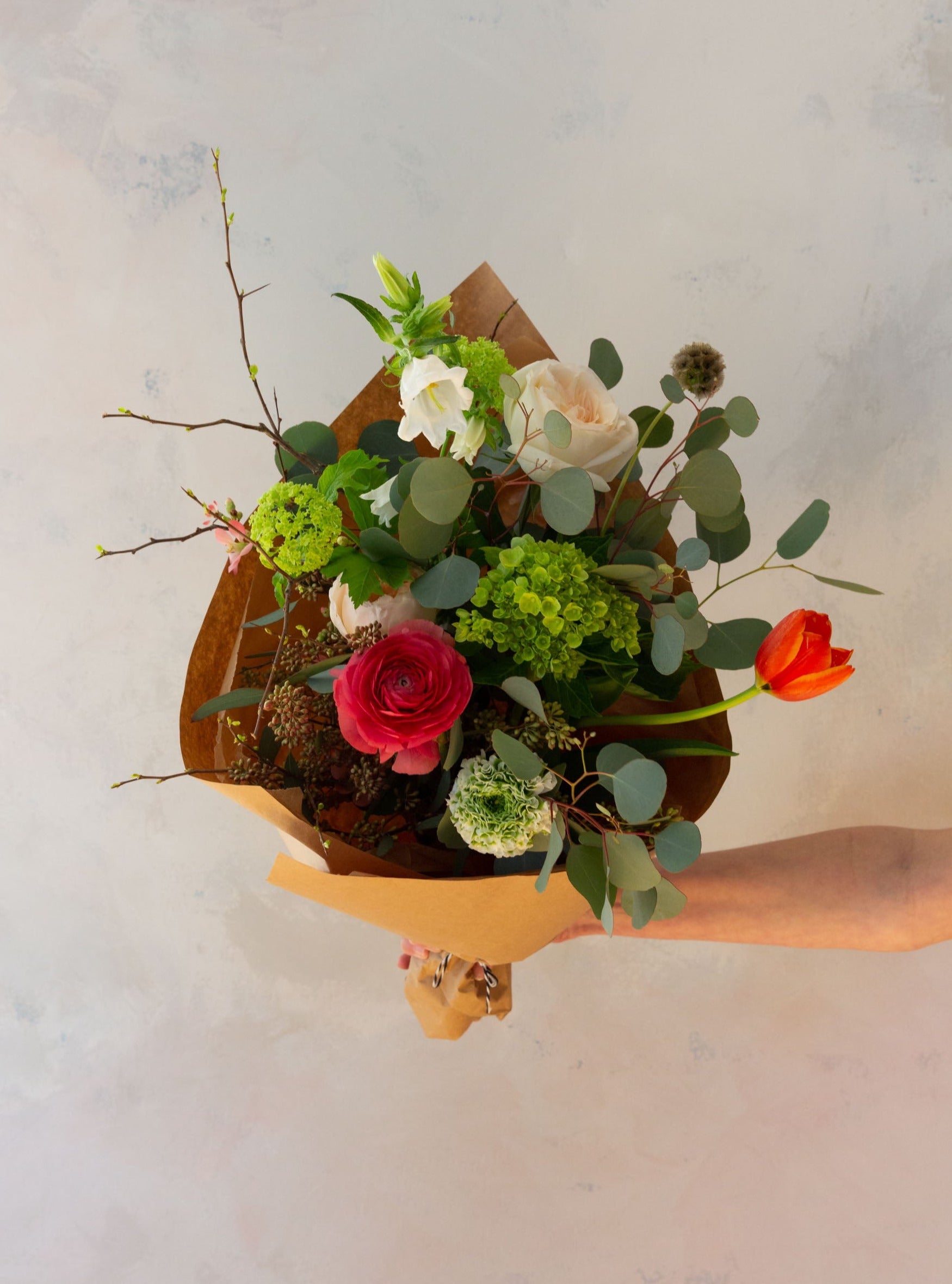 An arm holding an artfully designed wrapped floral bouquet 
