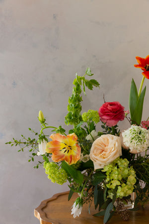 A close up view of a floral design of ranunculus, garden roses, tulips, viburnum and bells of Ireland