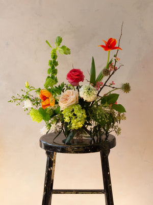 An artfully designed flower arrangement in a vessel against a neutral backdrop